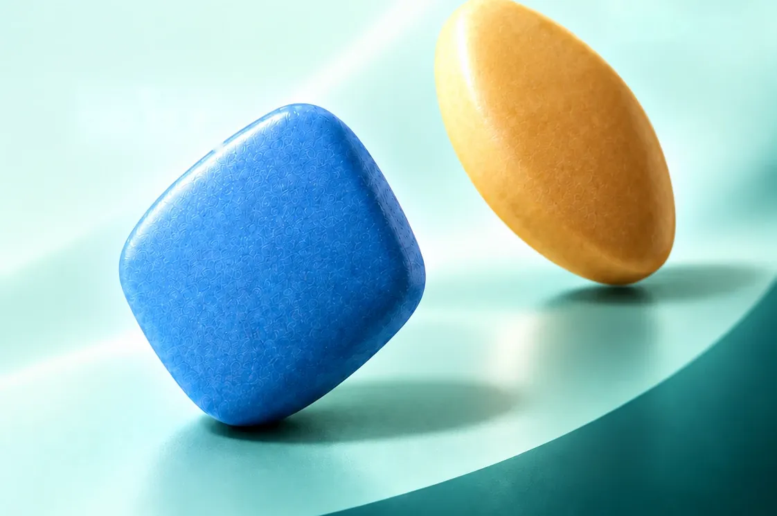 A blue diamond-shaped tablet and an amber oval tablet on a pale teal surface